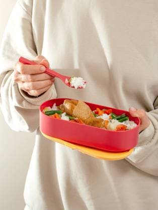 a girl eats food from a lunch box in the office. lunch box to th R_KUAL231016-1269580-01
