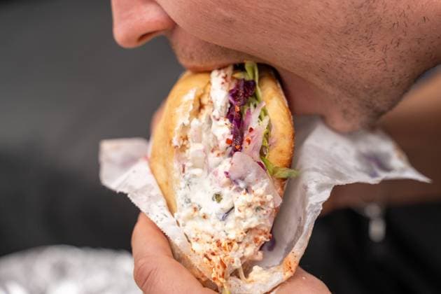 Augsburg, Bavaria, Germany - October 17, 2023: A man bites into a vegetarian kebab kebap without meat with lots of yogurt sauce *** Ein Mann beißt in einen vegetarischen Döner Kebap ohne Fleisch mit viel Joghurt Soße