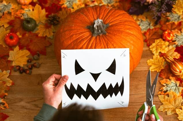 17 October 2023: decorate and carve a Halloween pumpkin. Man has ready knife and scissors and a template for a nasty Halloween face *** verzieren und schnitzen von einem Halloween Kürbis. Mann hält Messer und Schere bereit und eine Vorlage für ein fieses Halloween Gesicht