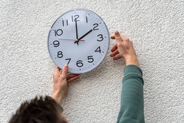 Augsburg, Bavaria, Germany - 17 October 2023: Man sets a clock hanging on the wall to winter time. Time change concept *** Mann stellt eine an der Wand hängende Uhr um auf Winterzeit. Zeitumstellung Konzept