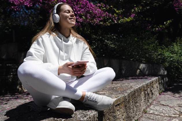 IMAGO Creative, Jahreszeit Frühling, Licht und Sonne Teenage girl listening music with headphones on wall at park model released, Symbolfoto, AAZF00761