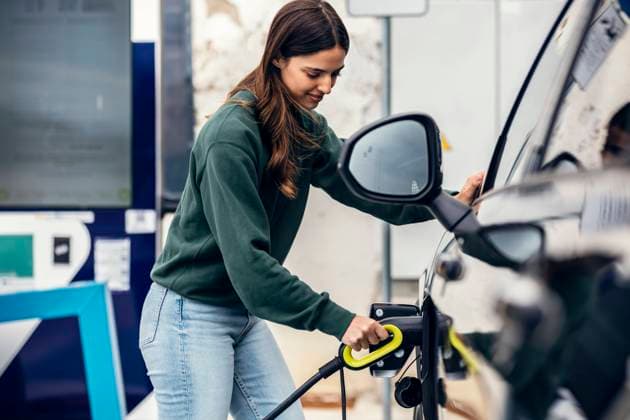Smiling woman plugging charger in car at electric vehicle charging station model released, Symbolfoto, JSRF02612