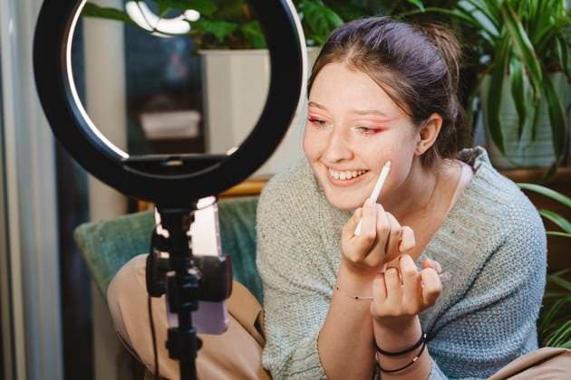 Smiling influencer streaming make-up video over mobile phone on balcony model released, Symbolfoto property released, IHF01752