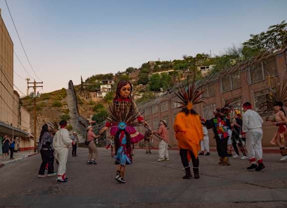 October 27, 2023, Nogales, Arizona, USA: Little Amal, the 12 foot puppet of a Syrian refugee girl is participates in a dance of welcome with young indigenous dancers. She is standing alongside a newly reconstructed border wall separating Nogales, Arizona and Nogales, Mexico. Nogales USA - ZUMAd155 20231027_znp_d155_010 Copyright: xSuexDorfmanx