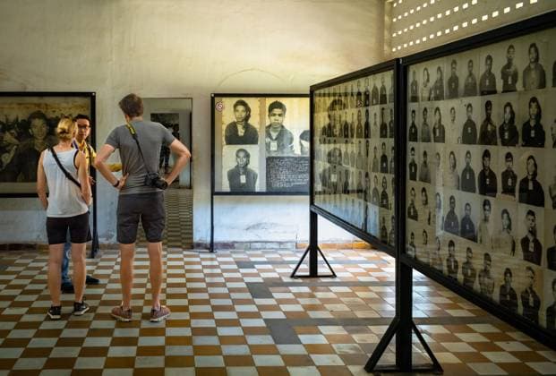 Two western tourists with their tour guide in a room at the Tuol Sleng, or S-21, torture and genocide museum in Phnom Penh, Cambodia, containing portraits of prisoners taken before they were murdered by the Khmer Rouge. Two western tourists with their tour guide in a room at the Tuol Sleng, or S-21, torture and genocide museum in Phnom Penh, Cambodia, containing portraits of prisoners taken before they were murdered by the Khmer Rouge. More than 18,000 people died here under the Khmer Rouge between 1975-79, and just 12 former prisoners survived. Copyright: AndyxSoloman 4063_09_AS_Tuol_12112022_012