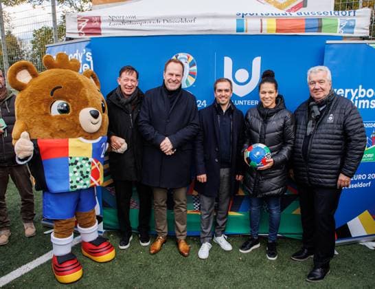 06.11.2023. Düsseldorf. Die UEFA EURO 2024 wird - getreu dem städtischen Motto Everybody s Heimspiel - zu einem Fußballfest für alle Düsseldorferinnen und Düsseldorfer. Die UEFA EURO 2024 soll auch über das Turnier hinaus nachhaltig sichtbare Spuren in der Stadt hinterlassen. Aus diesem Grund besucht Maskottchen Albärt (li.), Oberbürgermeister Dr. Stephan Keller (3. v. li.) zusammen mit Turnierdirektor und Fußball-Weltmeister Philipp Lahm (3. v. re.), Celia äaöic (Botschafterin und ehemalige Nationalspielerin, 2. v. re.), Peter Frymuth (Vizepräsident des Deutschen Fußballbundes und Präsident des Fußballverbandes Niederrhein, re.)) und Stadtdirektor Burkhard Hintzsche (2. v. li.) über 150 Nachwuchskickerinnen und -kicker beim SV Wersten. D