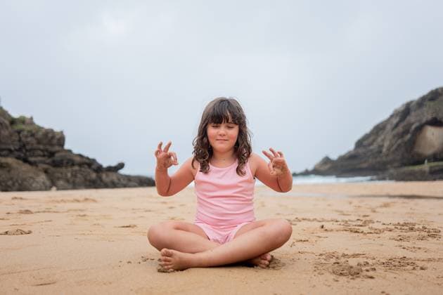 Creative Highlights Symbolbilder A cheerful young girl sits cross-legged on a beach, doing a yoga pose with a calm sea backdrop. Model Released HodeiUnzueta_ID17448_529618_006 Copyright: xHodeixUnzuetax RECORD DATE NOT STATED