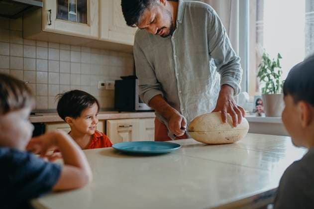 Father cutting melon with children at table in kitchen model released, Symbolfoto property released, ANAF02396