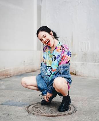 Creative Highlights Symbolbilder Young woman crouching on manhole and laughing in front of white wall model released, Symbolfoto, SVCF00395