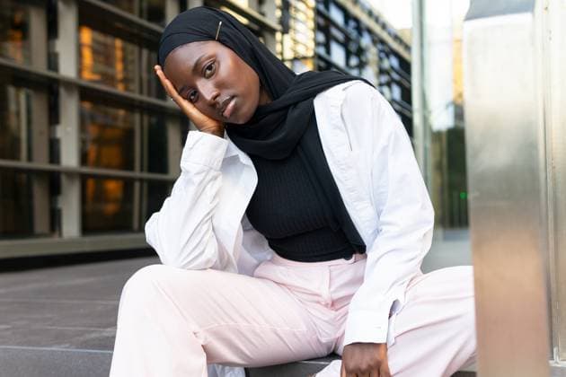 Creative Highlights Symbolbilder Serious emotionless young female Muslim entrepreneur in black headscarf and white formals touching face and sitting on street against building Model Released DavidMunoz_ID16772_512066_030 Copyright: xDavidxMunozx