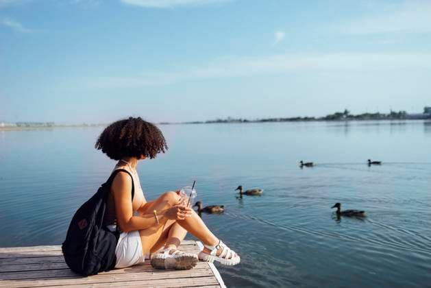 Beautiful mixed race female teenager sits on wooden pier and drinks cocktail in plactic glass. Charming african girl in casual clothes and with black backpack smiles sincerely near water. Sunny day. Beautiful mixed race female teenager sits on wooden pier and drinks cocktail in plactic glass. Charming african girl in casual clothes and with black backpack smiles sincerely near water. Sunny day. ,model released, Symbolfoto Copyright: xZoonar.com DashaxPetrenkox 20707055 ,model released, Symbolfoto ,property released