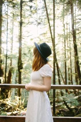 Creative Highlights Symbolbilder A peaceful moment captured as a woman in a white dress and black hat stands contemplatively in a sunlit forest on Avatar Grove, Vancouver Island. Model Released CamilleGirard_ID17696_535278_026 Copyright: xCamillexGirardx