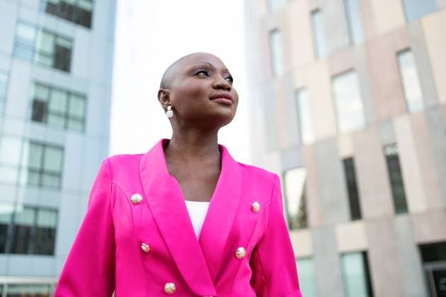 From below of Smiling African American female with shaved head in trendy pink suit standing on street and looking away while standing against buildings Model Released DavidMunoz_ID17368_528171_025 Copyright: xDavidxMunozx