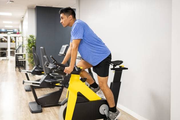 A focused man rides a stationary exercise bike in a well-equipped gym, displaying a healthy lifestyle practice. Model Released DavidMunoz_ID17833_538039_004 Copyright: xDavidxMunozx