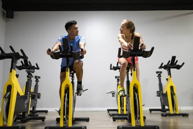 Two people engaged in a high-intensity workout on stationary bikes inside a gym, focusing on their fitness goals. Model Released DavidMunoz_ID17833_538070_021 Copyright: xDavidxMunozx