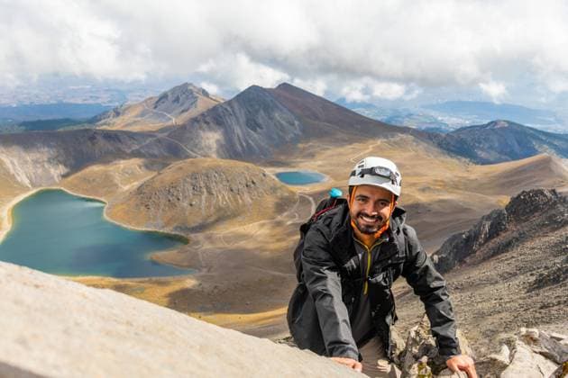 A smiling hiker wearing a helmet climbs Nevado de Toluca s rocky terrain with crater lakes in the background under a cloudy sky. Model Released EduardoGavira_ID17888_539292_004 Copyright: xEduardoxGavirax