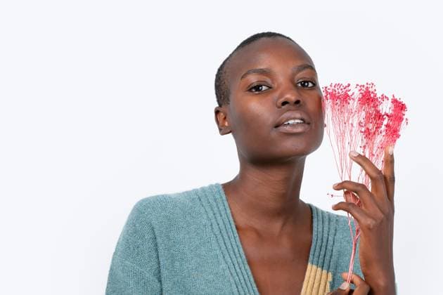 Creative Highlights Symbolbilder MR_ID17295_15546_ElisabetMoyua.jpg, MR_ID17295_15545_ShubilaStanton.jpg Thoughtful young bold African American female in blue sweater holding artificial pink plant decor looking at camera while standing on white background Model Released HodeiUnzueta_ID17295_526090_007 Copyright: xHodeixUnzuetax