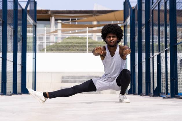 Full body of serious African American male athlete in activewear with hands clasped stretching leg and doing squatting against building in city Model Released MartinZubiriaPhotography_ID16842_514255_038 Copyright: xMartinxZubiriaxPhotographyx RECORD DATE NOT STATED