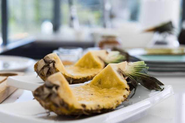 Cut pineapple pieces shell placed on kitchen table in daylight Appetizing fresh pineapple cut slices with thorny shell and green leaves while placed on white plate on kitchen table with ovary and core removed against blurred background Model Released MartinZubiriaPhotography_ID17004_518450_005 Copyright: xMartinxZubiriaxPhotographyx RECORD DATE NOT STATED