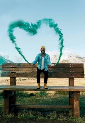 Creative Highlights Symbolbilder A joyful man stands on a bench while heart-shaped green smoke billows behind him in a scenic mountain landscape. Model Released SergioVictorVega_ID17966_541392_008 Copyright: xSergioxVictorxVegax