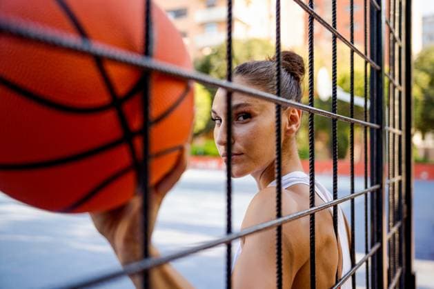 Creative Highlights Symbolbilder MR_ID16793_15544_LauraChahdour.jpg, MR_ID16793_15543_JoseHurtado.jpg Confident young female athlete in sportswear holding basketball looking at camera seen through fence of playground Model Released ValoaStudio_ID16793_512711_029 Copyright: xValoaxStudiox RECORD DATE NOT STATED