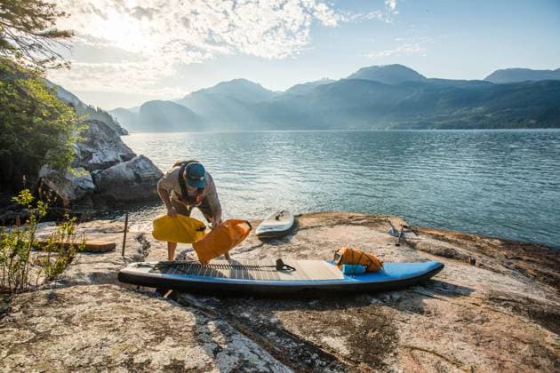 Man secures dry bags to paddle board, preparing for paddling trip Squamish, British Columbia, Canada CR_JDIP231218-1200123-01 ,model released, Symbolfoto