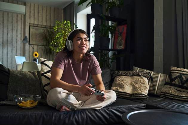 IMAGO Creative, Lifestyle, Gaming Happy young woman playing video game with controller on sofa at home model released, Symbolfoto property released, DSHF01146