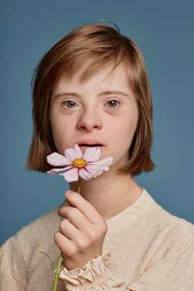 Creative Highlights Symbolbilder Girl with Down syndrome holding pink flower against blue background model released, Symbolfoto, KPEF00456