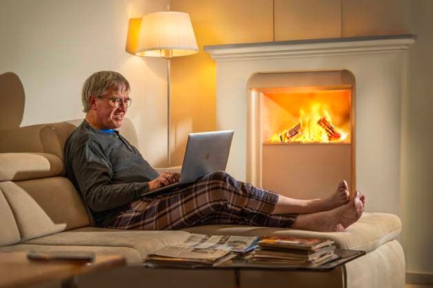 Mann sitzt abends allein zuhause gemütlich am Notebook, Kaminfeuer spendet wohlige Wärme, München, Januar 2024 Deutschland, München, Januar 2024, älterer Mann sitzt abends gemütlich am Notebook, surft im Internet, chattet mit Freunden, das Kaminfeuer spendet wohlige Wärme, er sitzt mit ausgestreckten Beinen auf dem Sofa, allein zuhause, Symbolfoto, Homeoffice, Winter, Bayern, *** Man sits comfortably at home alone in the evening at the notebook, fireplace provides cozy warmth, Munich, January 2024 Germany, Munich, January 2024, elderly man sits comfortably at the notebook in the evening, surfs the Internet, chats with friends, the fireplace provides cozy warmth, he sits with his legs stretched out on the sofa, alone at home, symbolic