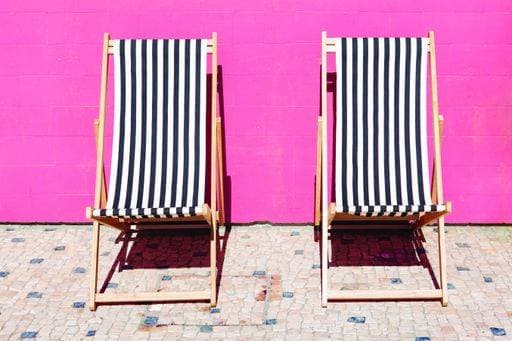 Black and white striped sun loungers against pink tile background 1948841
