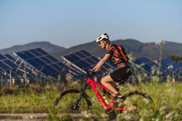 Side view of a beautiful cyclist riding in front of solar panels at a solar farm. Side view of a beautiful cyclist riding in front of solar panels at a solar farm during a summer bike tour in nature. A solar farm as solution for more sustainable energy future. model released Copyright: xx HHH SOLO TZ SOLAR ENERGY II 2023 HHH 012
