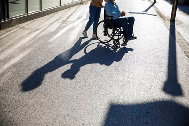 Caregiver pushing man in wheelchair on footpath with shadow model released, Symbolfoto, IKF01362