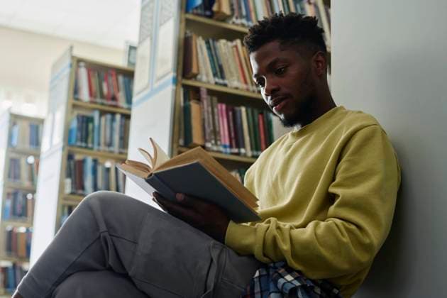 Student leaning on shelf and reading book in library model released, Symbolfoto property released, DSHF01501