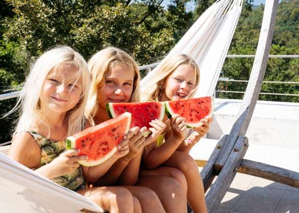 Smiling sisters sitting on hammock with slices of watermelons model released, Symbolfoto property released, NJAF00692