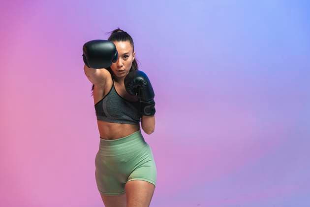 Creative Highlights Symbolbilder Confident young woman with black boxing gloves practicing against colored background model released, Symbolfoto, OIPF03693