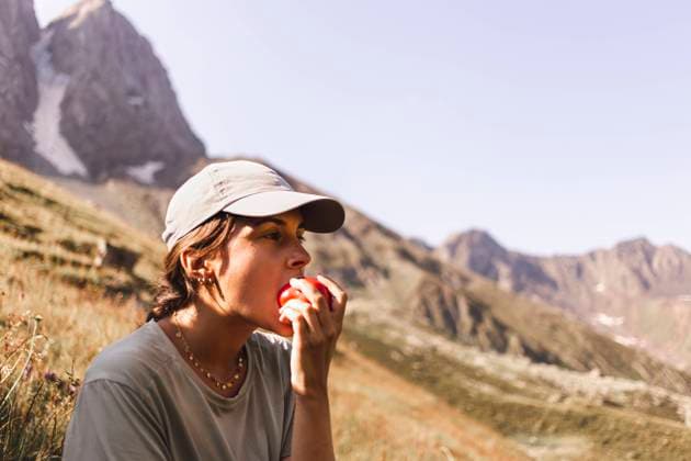 Woman wearing cap and eating tomato in front of mountains on sunny day model released, Symbolfoto, PCLF00956