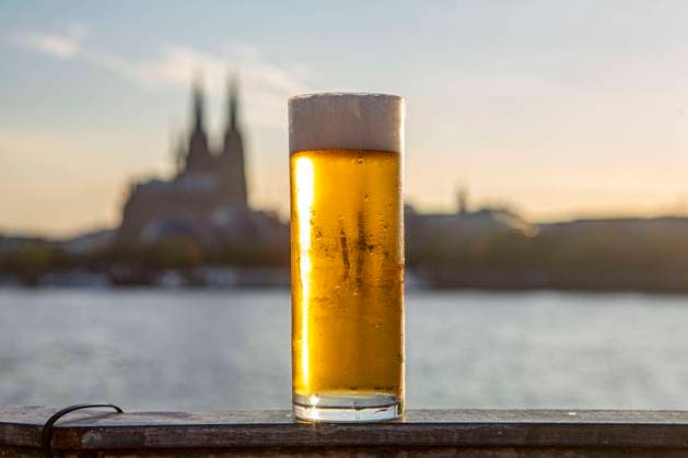 Ein Glas Kölsch steht am Rheinufer - im Hintergrund ist der Kölner Dom zu sehen. Kölsch *** A glass of Kölsch on the banks of the Rhine with Cologne Cathedral in the background Kölsch