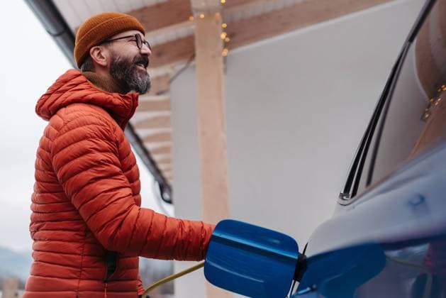 Man charging electric car during cold snowy day. Hansome man putting charger in charging port during winter, cold weather. Charging and driving electric vehicles during winter season. Man charging electric car during cold snowy day. Hansome mature man putting charger in charging port during cold weather. Charging and driving electric vehicles during winter season. Low angle shot. model released