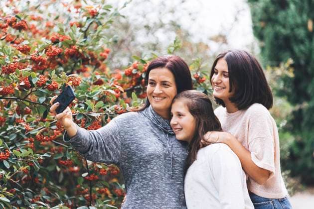 Mother and daughters smiling and taking selfie Lisbon, Portugal, 20.12.2023, model released, TTBB_ti0085_00536.jpg, Color Image,Horizontal,Outdoors,Day,Focus On Foreground,Selective Focus,Three People,People,14-15 Years,Teenager,Teenage Girls,16-17 Years,45-49 Years,Mid Adult,Mid Adult Women,Caucasian Appearance,Mother,Child,Family,Daughter,Girls,Sister,Smiling,Happiness,Brown Hair,Clear Sky,Sky,Bush,Plant,Flower,Red,Selfie,Photographing,Photography Themes,Holding,Smart Phone,Communication Copyright: xAlexandraxC.xRibeirox