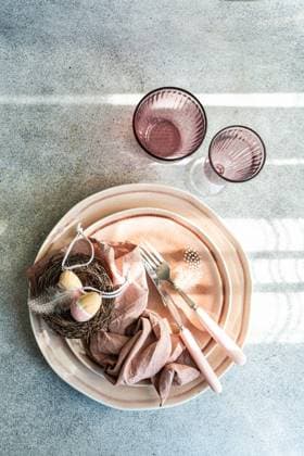 From above tasteful Easter table setting featuring pastel tableware and decorative eggs nestled in a small nest, accompanied by elegant cutlery. Model Released AnnaBogush_ID19406_575232_001 Copyright: xAnnaxBogushx