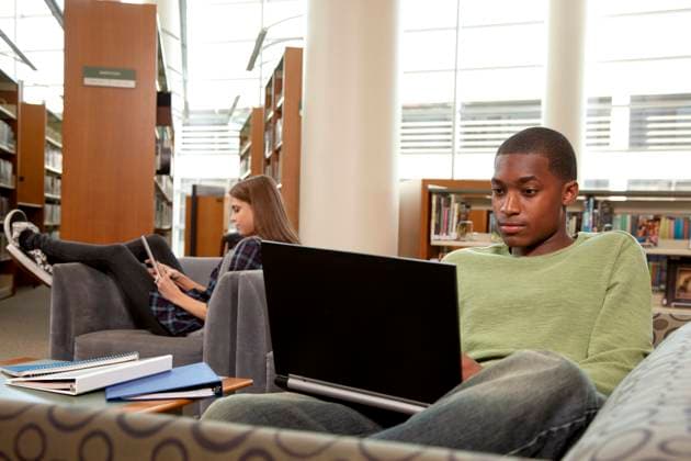 Student using laptop in a university library, lounging on couch. Dallas Texas United States  Copyright: xStewartxCohenxPicturesx 4009-19483085 ,model released, Symbolfoto