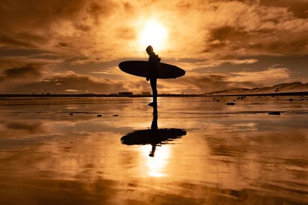 Creative Highlights Symbolbilder Woman standing on beach with surf board winter iceland sunset Grindavik, Grindavíkurbær, Iceland CR_ALEG240222-351822-01 ,model released, Symbolfoto