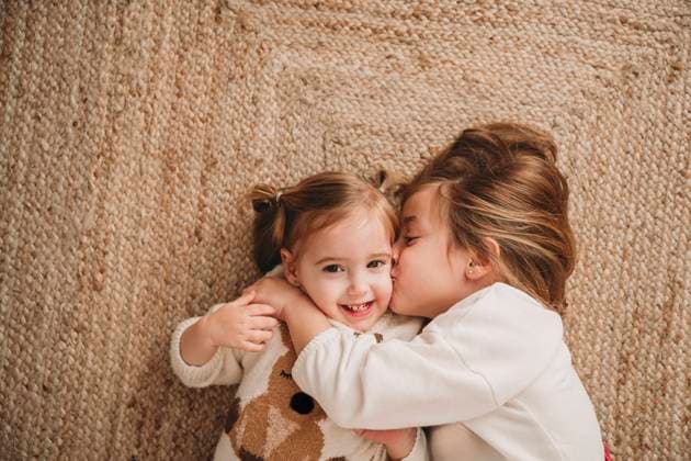Girl kissing smiling sister lying on carpet at home model released, Symbolfoto property released, EBBF08337