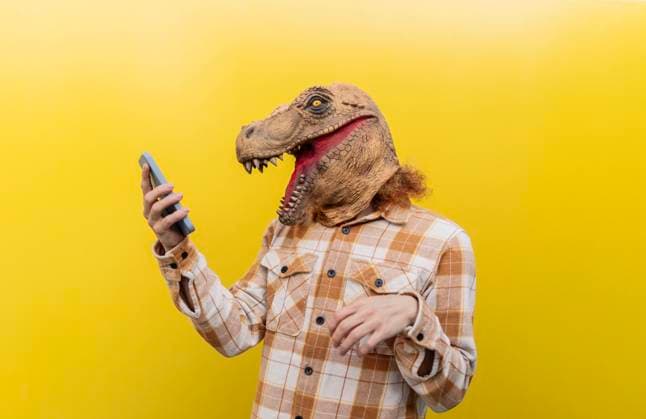 Creative Highlights Symbolbilder Man wearing dinosaur mask and using smart phone in front of yellow wall model released, Symbolfoto, JCCMF11164