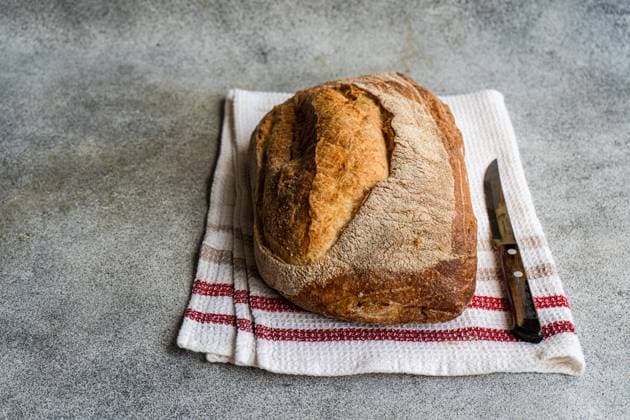 Top view of golden-brown rye sourdough bread on a white cloth with red stripes, next to a bread knife on a textured surface Model Released AnnaBogush_ID19733_585087_007 Copyright: xAnnaxBogushx