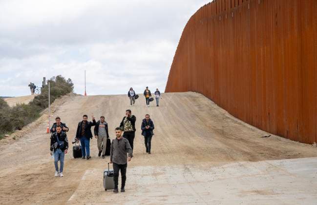 Migrants walk along the United States side of the border wall with Mexico to surrender to the U.S. Border Patrol near Campo, California on March 13, 2024. A bipartisan Senate immigration bill to address the migrant immigration issue is stalled in the House due to election year politics.  CAL2024031402 PATxBENIC