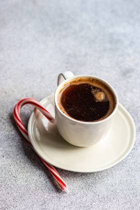 A cozy morning scene featuring a white mug of hot coffee paired with a red and white candy cane on a speckled grey surface. Model Released AnnaBogush_ID20069_593794_004 Copyright: xAnnaxBogushx