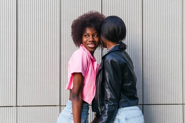 Creative Highlights Symbolbilder Two sisters share a joyful moment, with one looking back and smiling at the camera, showcasing a casual, trendy look against a modern metal backdrop Model Released DavidMunoz_ID19789_587091_001 Copyright: xDavidxMunozx