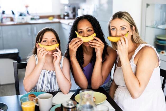 IMAGO Creative, Diversity, Familie: Gleichgeschlechtliche Eltern: Zwei Mütter Playful family holding banana near mouth at home model released, Symbolfoto property released, WPEF08395