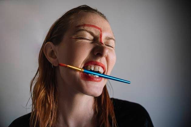 Creative Highlights Symbolbilder Woman holding paintbrush in mouth against gray background model released, Symbolfoto property released, ASHF00079